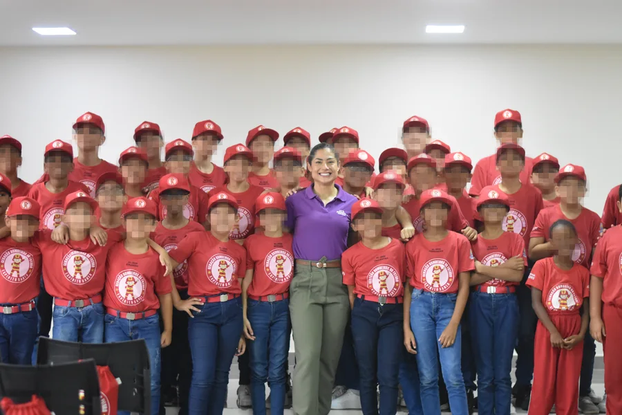 Andresa cercada por dezenas de crianças de camiseta e boné vermelhos, num encontro de formação.