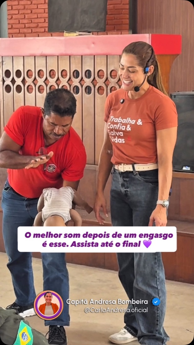 Andresa num palco, ensinando a manobra de desengasgo a um homem que segura um manequim de bebê.