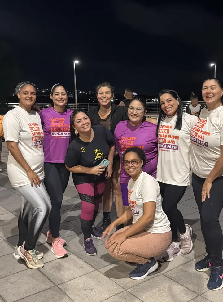 Andresa no meio de um grupo grande de mulheres, todas sorrindo, depois de um treino à noite.